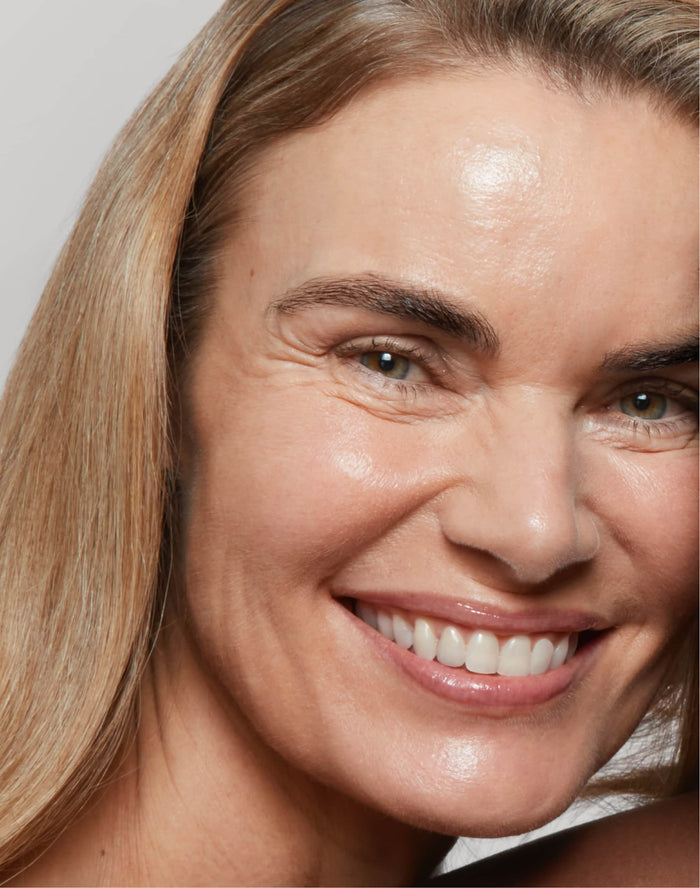 Primer plano de una mujer sonriente con pelo rubio liso y piel clara, mostrando belleza natural y cuidado facial antiedad.